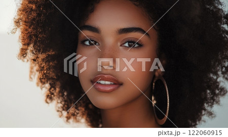 A young woman with curly hair and hoop earrings smiles warmly, showcasing her natural beauty in bright outdoor light. 122060915