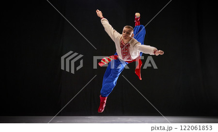 Male dancer in traditional Ukrainian attire, performing dance moves, showcasing strength and acrobatics of Hopak, against black studio background. Male dancer in traditional Ukrainian attire, performing dance moves, showcasing strength and acrobatics of Hopak, against black studio background. 122061853