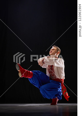 Group of dancers performing intricate footwork, dressed in traditional embroidered shirts, moving with rhythm and energy to showcase traditions against black studio background. 122061904