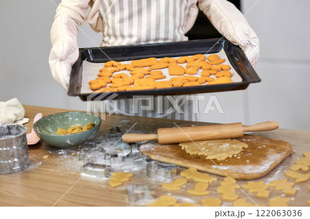 housewife woman in apron holds cookies on baking tray in kitchen 122063036
