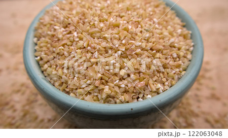 Broken Crushed Wheat (Dalia) in a Blue Bowl Isolated on Wooden Background Broken Crushed Wheat (Dalia) in a Blue Bowl Isolated on Wooden Background 122063048