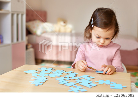 Cute little child girl connecting puzzle pieces on wooden desk in room Cute little child girl connecting puzzle pieces on wooden desk in room 122063092