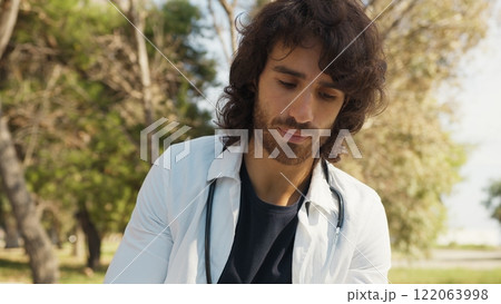 Male Doctor Writes Patient's Medical Record Outside In Hospital Park Among Trees 122063998