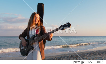 Girl Walks And Plays The Bass Instrument On The Beach Near The Ocean At Sunset Girl Walks And Plays The Bass Instrument On The Beach Near The Ocean At Sunset 122064013