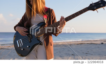 Girl Plays Bass Music Instrument On The Beach At Sunset Near Ocean Girl Plays Bass Music Instrument On The Beach At Sunset Near Ocean 122064018