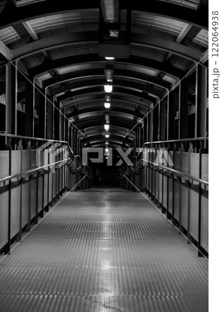 Pedestrian bridge with a metallic walkway and arched overhead structure at night Pedestrian bridge with a metallic walkway and arched overhead structure at night 122064938