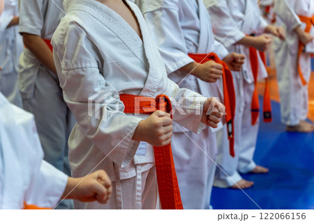 A close-up of a row of young athletes in white karate kimonos with clenched fists. 122066156