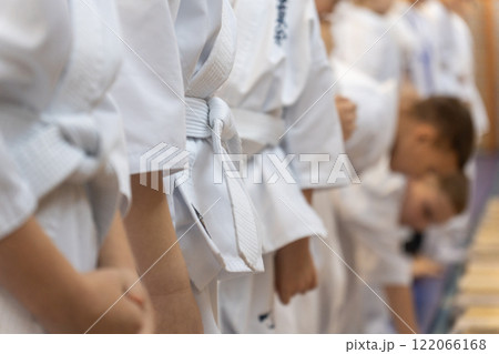A close-up of a row of young athletes in white karate kimonos with clenched fists. 122066168