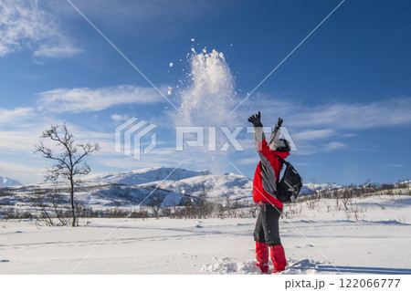 Sporty person in red sport jacket enjoys snow and breathtaking Norwegian landscape. Sunny winter activity. 122066777