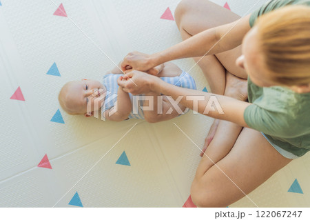 A mother practices baby gymnastics with her 3-month-old on a soft children's play mat. A joyful and nurturing moment focused on bonding, development, and care. Early childhood, fitness, and parenting A mother practices baby gymnastics with her 3-month-old on a soft children's play mat. A joyful and nurturing moment focused on bonding, development, and care. Early childhood, fitness, and parenting 122067247