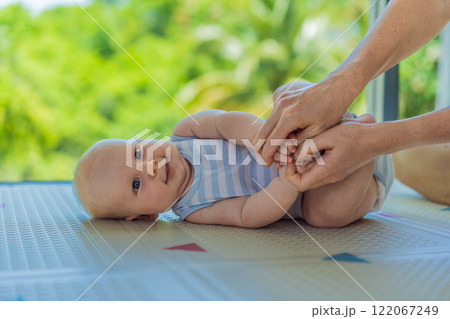 A mother practices baby gymnastics with her 3-month-old on a soft children's play mat. A joyful and nurturing moment focused on bonding, development, and care. Early childhood, fitness, and parenting A mother practices baby gymnastics with her 3-month-old on a soft children's play mat. A joyful and nurturing moment focused on bonding, development, and care. Early childhood, fitness, and parenting 122067249