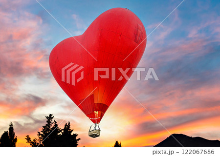 Red heart shaped hot air balloon flying over sunset sky	 122067686