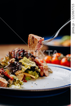 Fork lifting seared tuna over fresh salad, a perfect blend of healthy and gourmet dining Fork lifting seared tuna over fresh salad, a perfect blend of healthy and gourmet dining 122067715