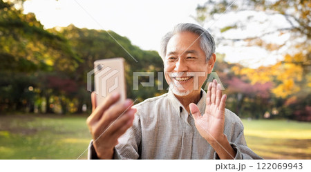 公園でスマートフォンを使ってビデオ通話しているシニア男性。 公園でスマートフォンを使ってビデオ通話しているシニア男性。 122069943