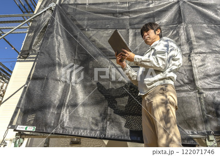 戸建て家屋の外壁修繕工事進行状況を確認する男性 122071746