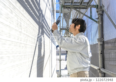 戸建て家屋の外壁修繕工事進行状況を確認する男性 122072948