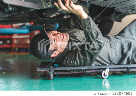 メカニッククリーパーに乗り車の下回りをチェックする自動車整備士の男性 122074602
