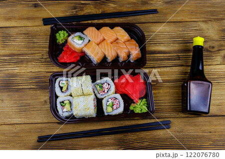 Set of sushi rolls in plastic boxes, soy sauce and chopsticks on wooden table. Top view. Sushi for take away or delivery of sushi in plastic containers 122076780