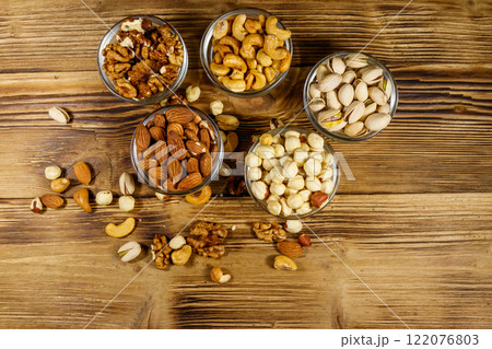 Assortment of nuts on wooden table. Almond, hazelnut, pistachio, walnut and cashew in glass bowls. Top view. Healthy eating concept 122076803