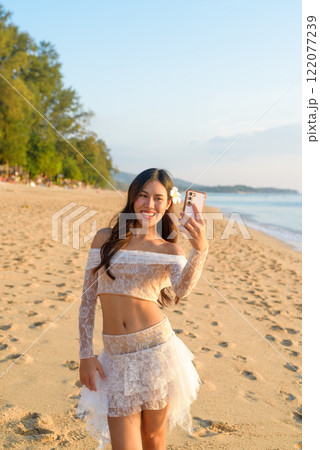 Happy Young Woman Taking Selfie with Vibrant Ocean Sunset Background Happy Young Woman Taking Selfie with Vibrant Ocean Sunset Background 122077239