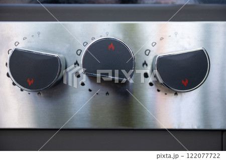 A closeup view of sleek stainless steel stove knobs featured prominently in a modern kitchen 122077722