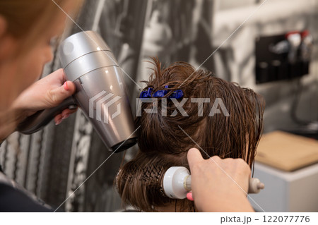 A skilled stylist uses a highquality hairdryer in a modern salon, showcasing their expertise A skilled stylist uses a highquality hairdryer in a modern salon, showcasing their expertise 122077776