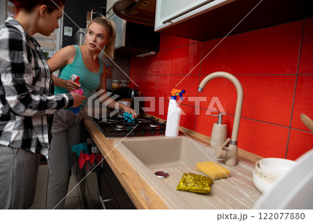 Two women are joyfully cleaning the kitchen together, showcasing their teamwork and care 122077880