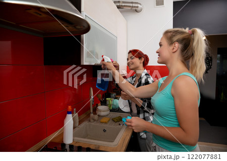 Two women are enthusiastically cleaning together in a bright and modern kitchen space 122077881