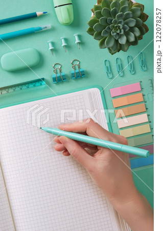 Woman's hand writes in a notebook with turquoise stationery on a mint background Woman's hand writes in a notebook with turquoise stationery on a mint background 122078257