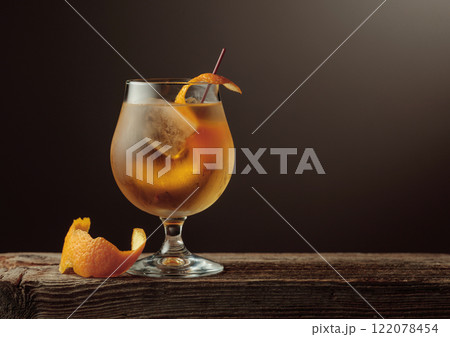 Old Fashioned cocktail with a ice, garnished with an orange peel on a old wooden board. Old Fashioned cocktail with a ice, garnished with an orange peel on a old wooden board. 122078454