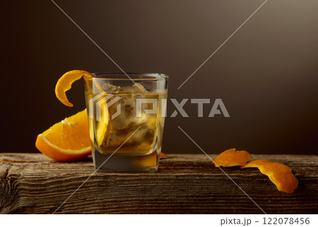 Old Fashioned cocktail with a ice, garnished with an orange peel on a old wooden board. 122078456