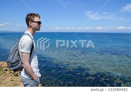 Young Russian man in sunglasses enjoying the view of the Sea of Japan on the Far East coast of Russia. Clear blue sky and calm water create a tranquil atmosphere 122080482