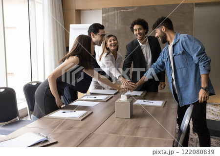 Five multiethnic teammates stack their palms together, celebrate achievements 122080839