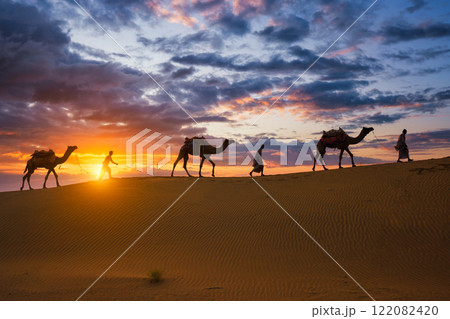 Indian cameleers camel drivers camel silhouettes in dunes on sunset. Jaisalmer, Rajasthan, India Indian cameleers camel drivers camel silhouettes in dunes on sunset. Jaisalmer, Rajasthan, India 122082420
