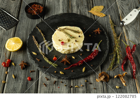 A beautifully arranged platter showcases a round cheese topped with herbs and spices on a grey kitchen table 122082785