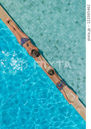 A mother and her son relax at the edge of clear blue pool during sunny summer vacation. This aerial view captures family bonding, fun, and recreation at resort, relaxation and joyful outdoor moments. 122085462