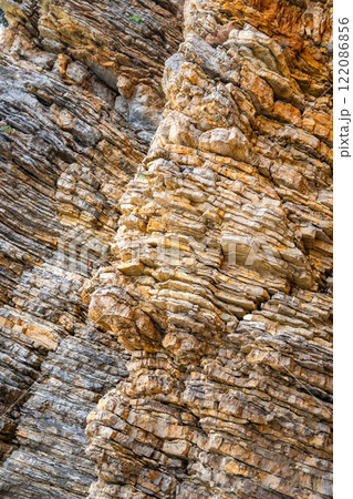 Layered rock texture in Budva, Montenegro. Sedimentary rocks with rugged surface of gray and brown. Natural formation of layers and cracks, geological structure. Layered rock texture in Budva, Montenegro. Sedimentary rocks with rugged surface of gray and brown. Natural formation of layers and cracks, geological structure. 122086856