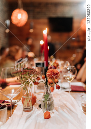 Elegant table centerpiece with red candles, flowers, and glassware at a festive dinner gathering Elegant table centerpiece with red candles, flowers, and glassware at a festive dinner gathering 122088290