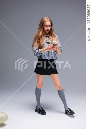 A Trendy Young Girl Dressed in Stylish and Chic Attire, Holding a Smartphone in a Creative Manner A Trendy Young Girl Dressed in Stylish and Chic Attire, Holding a Smartphone in a Creative Manner 122089037
