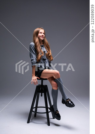 A Charming Fashion Model Posing Elegantly on a Stylish Stool Wearing a Trendy Outfit A Charming Fashion Model Posing Elegantly on a Stylish Stool Wearing a Trendy Outfit 122089039