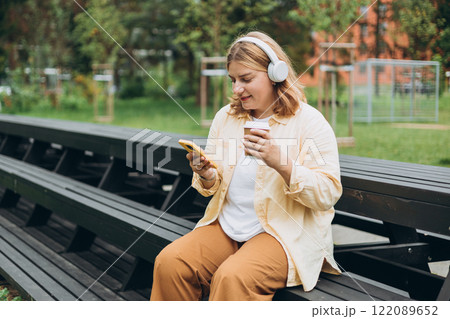 Closeup portrait of a lovely young female listening to music through wireless earphones on nature background. Music lover enjoying music. Woman record voice by mobile cell phone Dictaphone 122089652