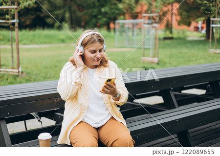 Closeup portrait of a lovely young female listening to music through wireless earphones on nature background. Music lover enjoying music. Woman record voice by mobile cell phone Dictaphone 122089655