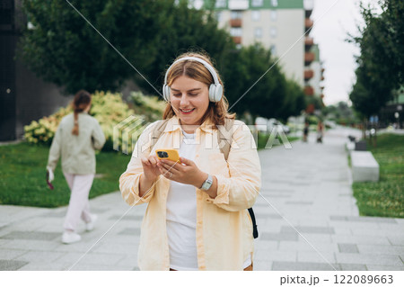 Closeup portrait of a lovely young female listening to music through wireless earphones on urban background. Music lover enjoying music. Woman record voice by mobile cell phone Dictaphone Closeup portrait of a lovely young female listening to music through wireless earphones on urban background. Music lover enjoying music. Woman record voice by mobile cell phone Dictaphone 122089663