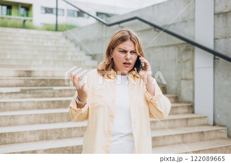 Angry woman on cell phone walking outside building near steps. Frustrated woman talking on phone. Summer time. Negative people emotion 122089665