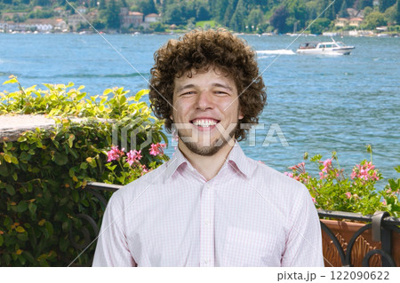 Portrait of a cheerful happy man with curly hair on vacation. Summer lake in the background. 122090622