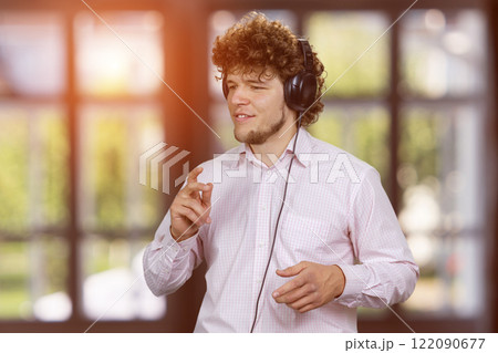 Happy young guy enjoying music in headphones. Checkered indoor window in the background. 122090677