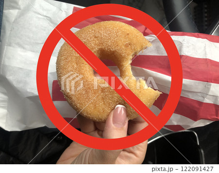 Donut held in hand with a red prohibition sign symbolizing unhealthy eating or sugar-free diet concept Donut held in hand with a red prohibition sign symbolizing unhealthy eating or sugar-free diet concept 122091427