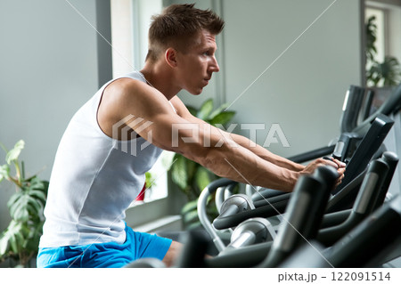 Young muscular man on exercise bike in gym Young muscular man on exercise bike in gym 122091514