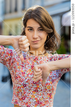 Upset young woman showing thumbs down sign, disapproval, dissatisfied bad work, mistake in city 122093050