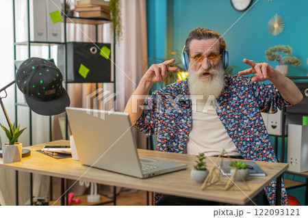 Happy senior man listening music through wireless headphones relaxing taking a break with laptop 122093121